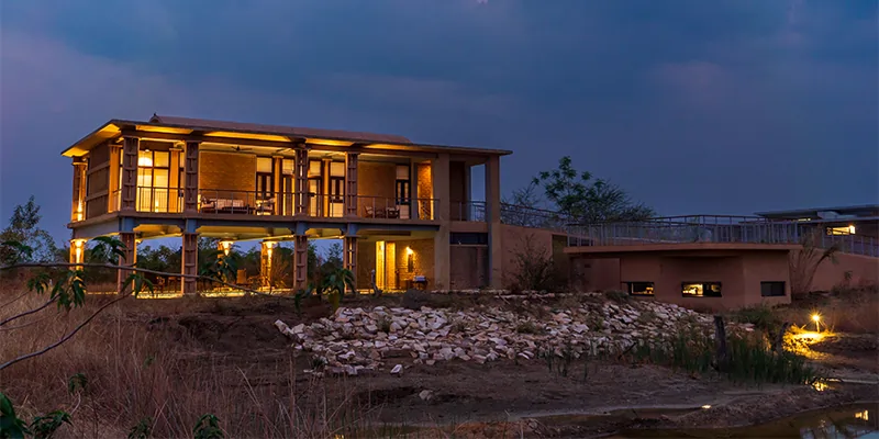 Luxury eco lodge exterior illuminated at dusk beside a lake in Tadoba